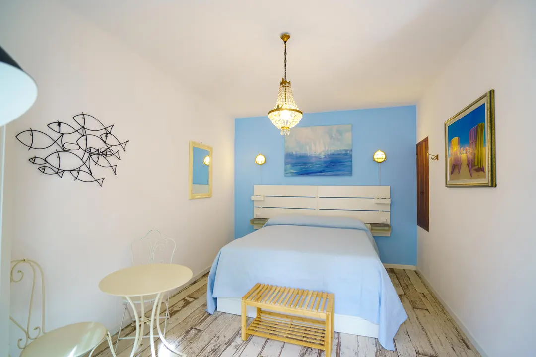 Camera matrimoniale con parete azzurra, quadro marino e lampadario di cristallo