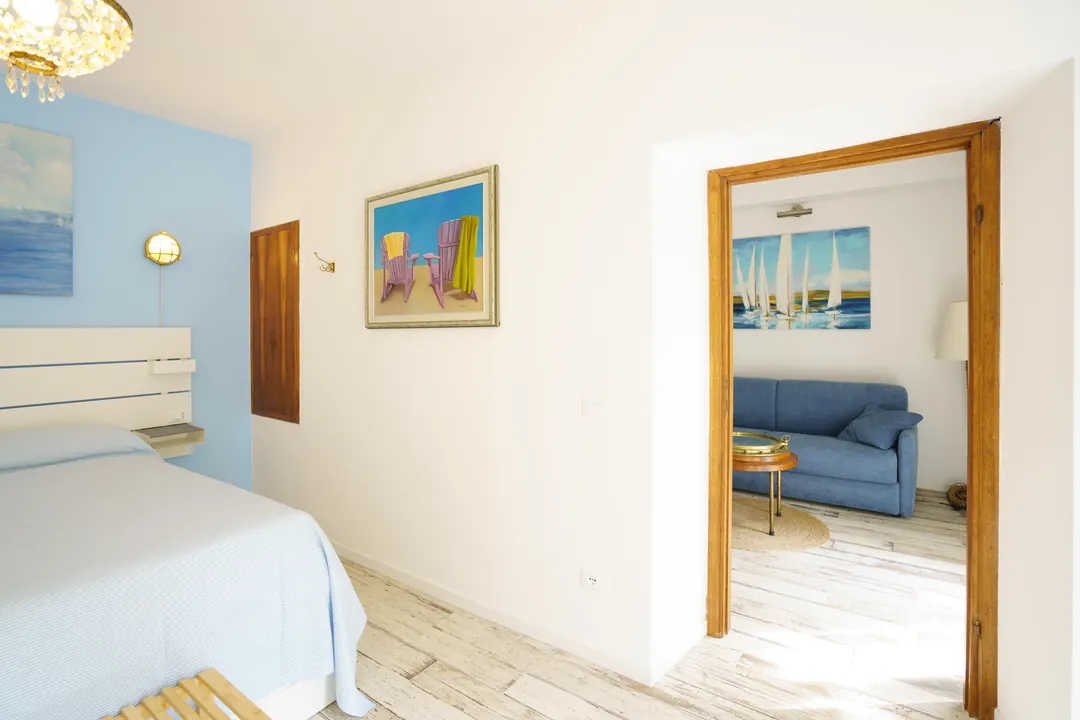 Camera con la parete azzurra; dalla porta aperta si vedono il soggiorno e un quadro di vele